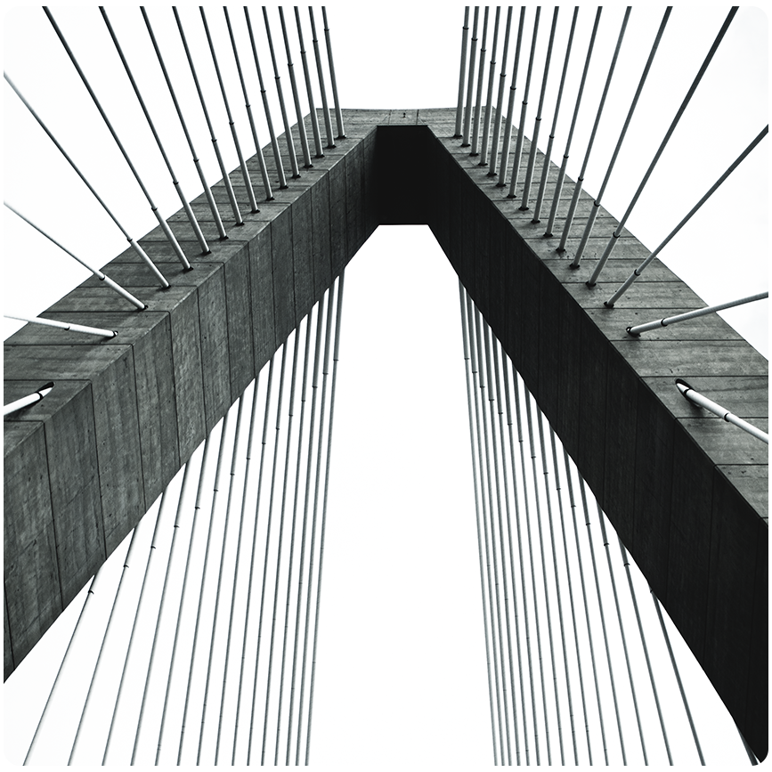 Symmetrical low-angle black-and-white shot looking up between two concrete bridge pylons with cable stays converging into the sky