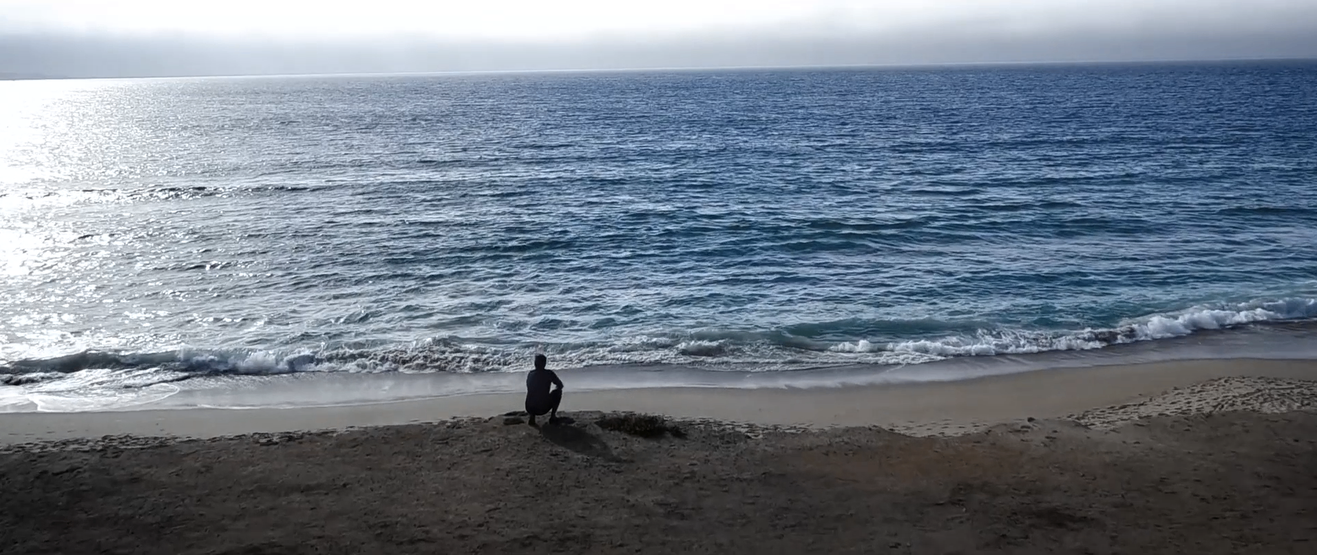 Solitary figure seated above the shoreline looking out across the ocean