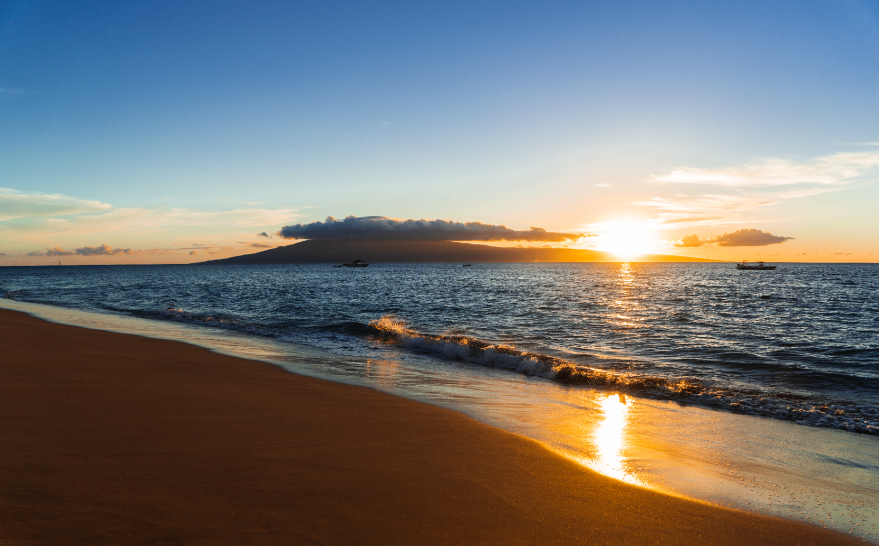 Warm sunset over a calm shoreline with an island on the horizon and golden reflections across the wet sand