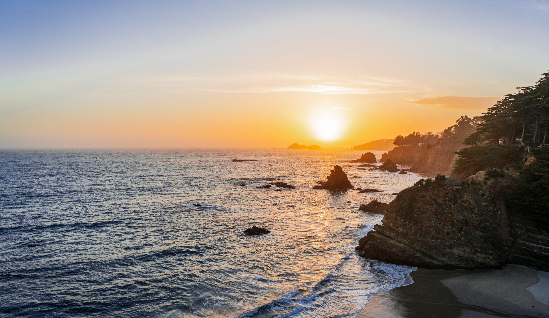 Golden sunset dropping into the Pacific beside dark cliff edges and sea stacks on the Sea Ranch coastline