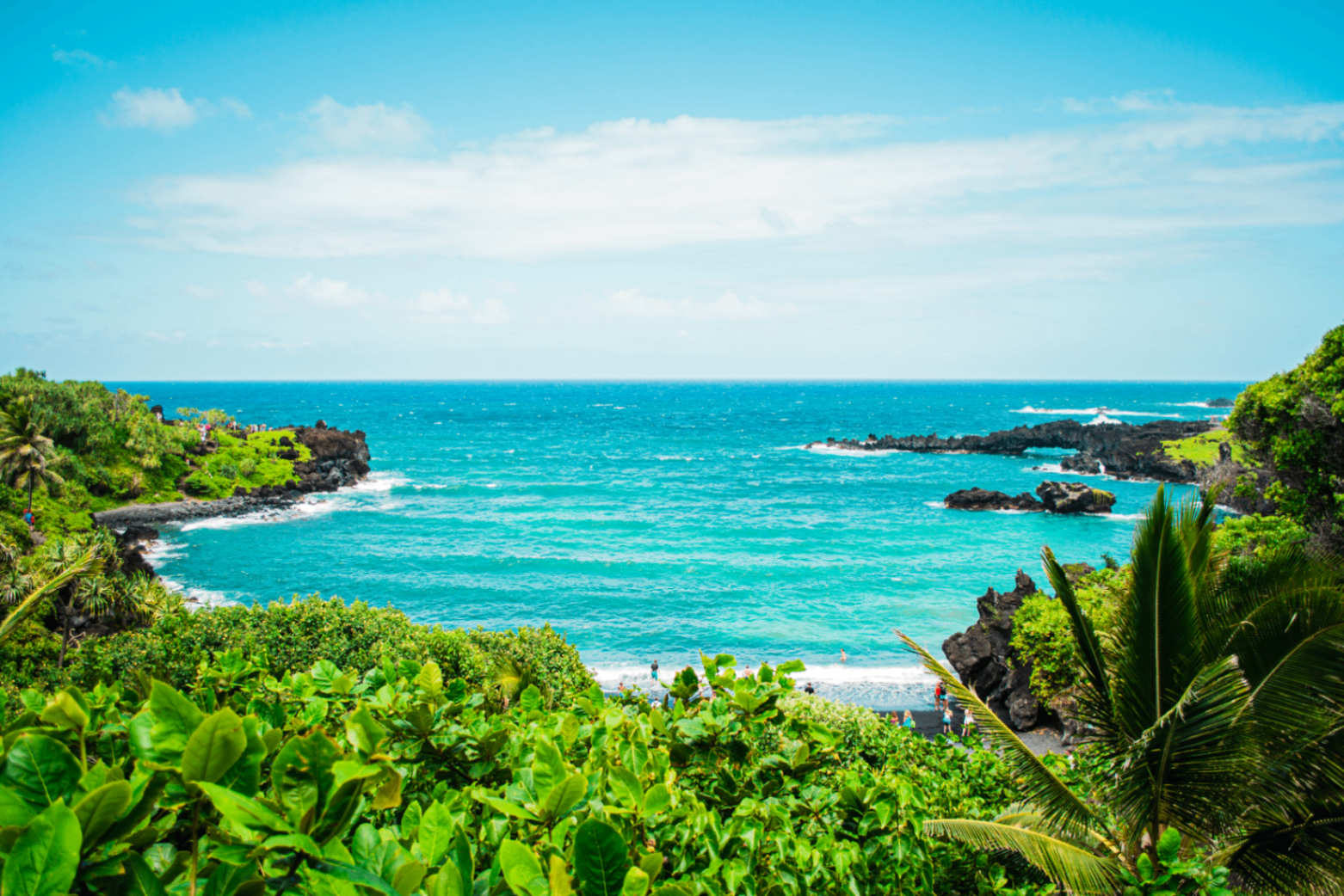 View over lush greenery toward a bright turquoise bay framed by dark volcanic rock