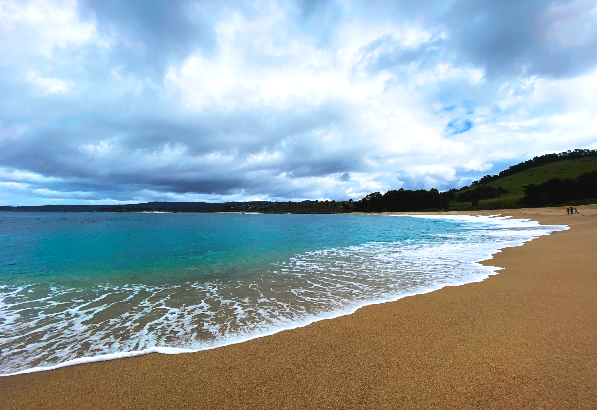 Turquoise water curling onto a broad sandy beach beneath heavy coastal clouds at Sea Ranch