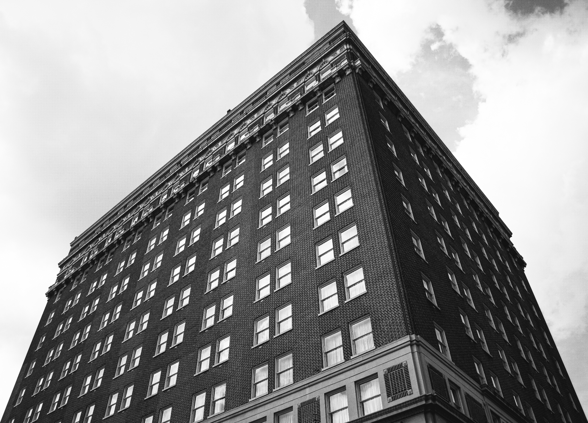 Low-angle black-and-white photograph of an early-20th-century brick high-rise against a cloudy sky