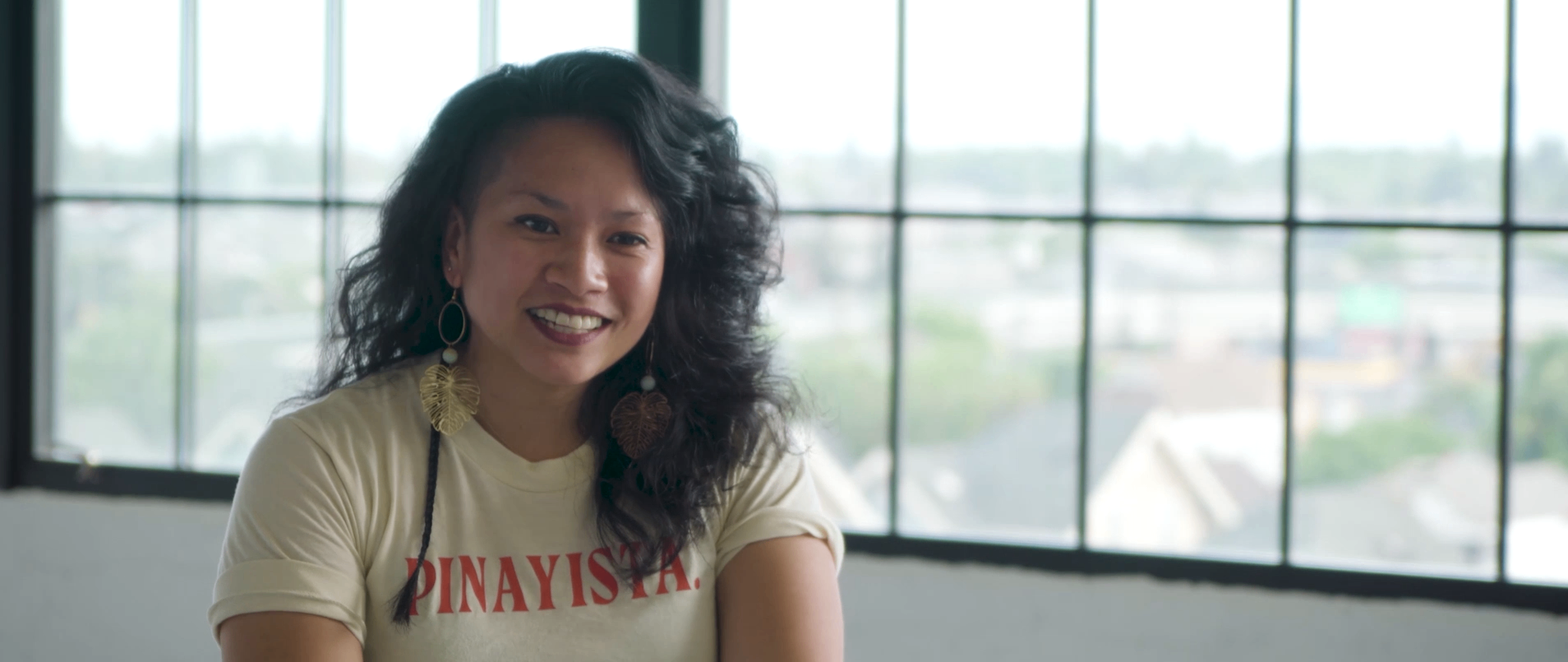 Portrait interview frame of a smiling subject seated against a large window