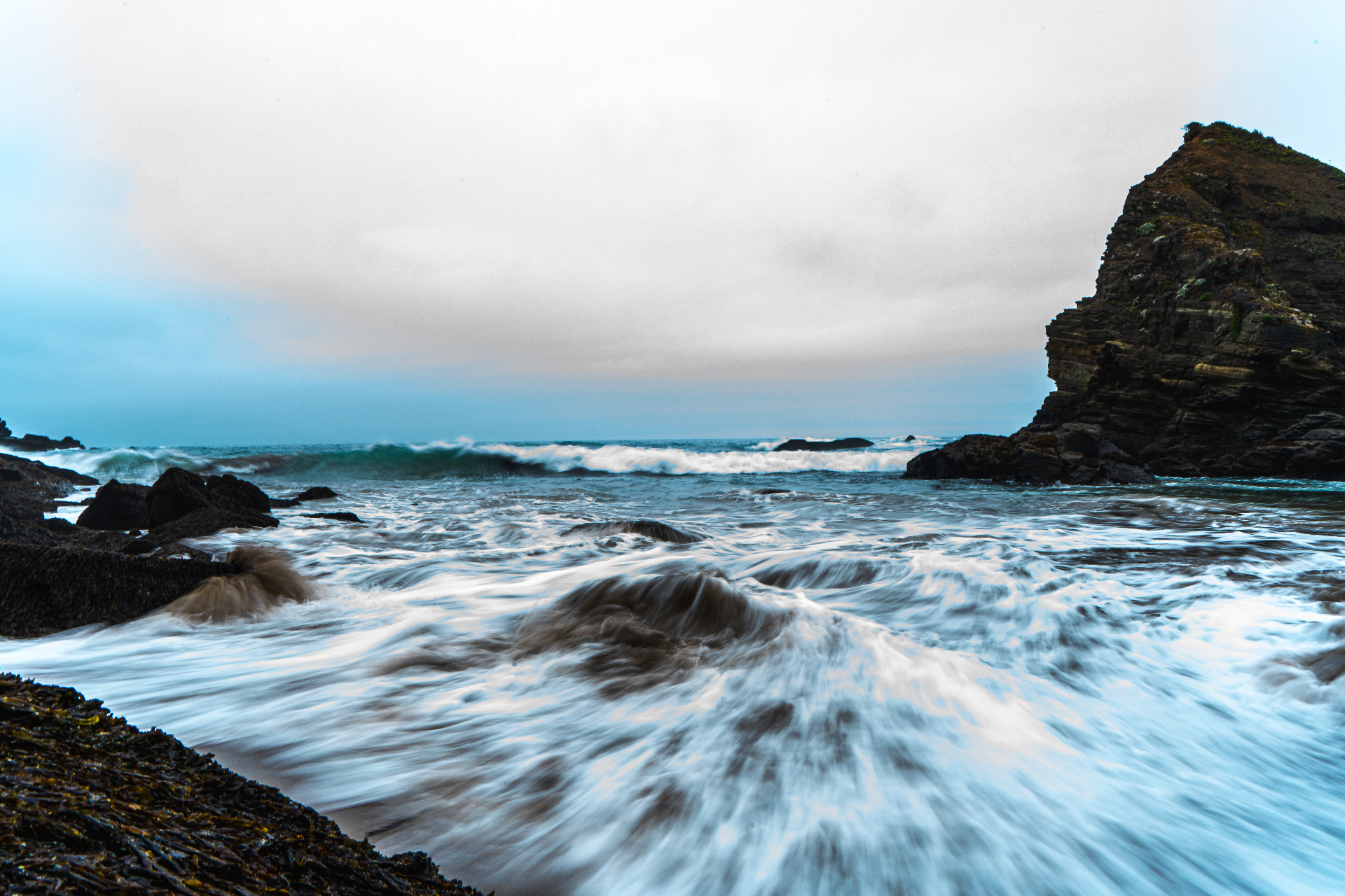 Long-exposure of waves rushing through a rocky cove beneath a moody overcast sky